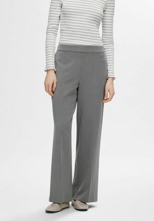 Grau maßgeschneiderte Hose mit geradem Bein, aus einem glatten Stoff gefertigt. Kombiniert mit einem grau-weiß gestreiften Langarmoberteil.