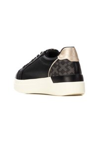 Zapatilla negra con material texturizado, talón con acentos en dorado en contraste y suela blanca. Presenta lados con patrón y parte delantera con cordones.