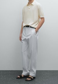 Polo crème, pantalon blanc ample, ceinture noire et sandales noires à enfiler. Texture lisse, design décontracté, palette de couleurs minimaliste.