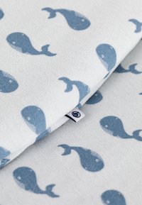 Katoenen stof met een lichtgrijze achtergrond en blauwe walvispatronen. In één hoek is een klein, gestikt merklabel zichtbaar.