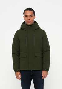 Giacca padded verde scuro con cappuccio, due tasche frontali e tasche sul petto con zip. Dotata di polsini regolabili e una finitura liscia.