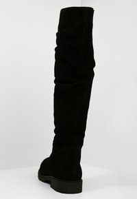 Mustat ylipolvensaappaat, jotka on valmistettu pehmeästä sametista, slouchy-muotoilulla ja tasapohjaisella kumipohjalla mukavuutta varten.