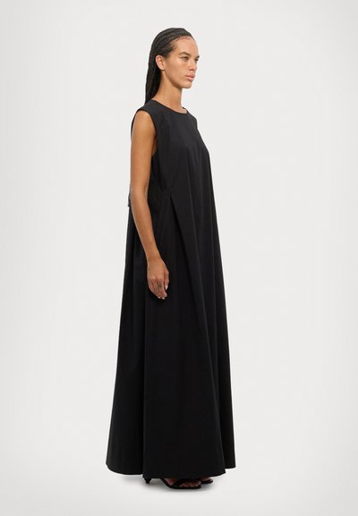 Robe maxi noire sans manches, avec une coupe ample, fabriquée en tissu doux. Présente des plis latéraux et un détail de fermeture éclair latérale discrète.