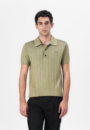 Short-sleeve polo shirt in olive green, featuring ribbed texture, three-button placket, and a subtle logo on the chest.