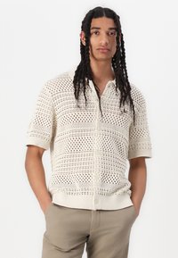 Camicia a maniche corte con bottoni in maglia aperta di colore crema, caratterizzata da un motivo testurizzato, colletto alla francese e polsini e orlo a coste.