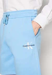 Light blue cotton shorts with a ribbed waistband, drawstring closure, and embroidered Calvin Klein Jeans logo on the left front pocket.