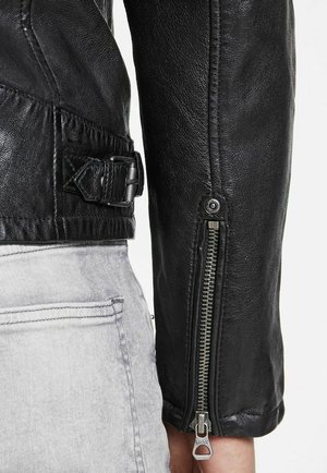 Czarna skórzana kurtka z zapinanym na zamek mankietem, o fakturowanym wykończeniu, z regulowanym paskiem i srebrnymi detalami sprzętowymi.