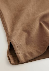 Bruine stof met een zachte textuur, gevouwen en met een naaddetail zichtbaar. Het materiaal lijkt glad met een matte afwerking en heeft een lichte kreuk.