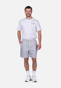 Weißes T-Shirt mit Logo, kombiniert mit hellgrauen gestreiften Shorts mit elastischem Bund und Zugband. Tragen mit weißen Sneakern.