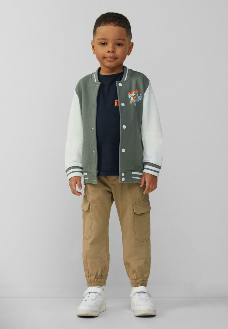 Groen en witte varsityjack met drukknoopsluiting, marineblauw T-shirt, khaki cargobroek en witte sneakers. Bevat geborduurd ontwerp.