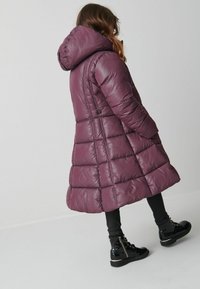 Lila puffiga jacka med huva, med kviltade sektioner och sidofickor. Matchad med svarta leggings och glänsande svarta ankelstövlar.