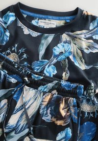 Zestaw loungewear w kwiaty w ciemnonawowym kolorze z niebieskimi i kremowymi wzorami kwiatowymi. Posiada elastyczny pas i miękki, gładki materiał.