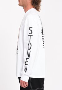 Hvid langærmet t-shirt med sort tekst "STONE" på ærmet, grafisk design på forsiden og et logo på den nederste ærme.