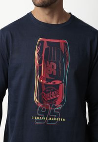 Camisa de manga larga azul marina que presenta un gráfico colorido de un auto de carreras con el número 95 y la marca "Rust-eze" en la parte frontal.