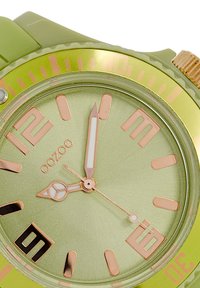 Green silicone watch with a gold-tone bezel, a matte green dial, large rose-gold hour markers, white hands, and a date window at 6.
