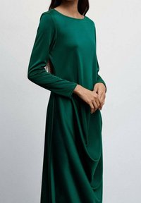 Langärmliges Kleid in Dunkelgrün, glattes Material mit rundem Halsausschnitt und Drapierung in der Taille. Minimalistisches Design.