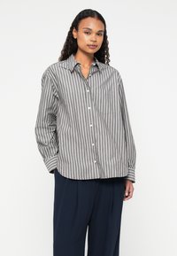 Camicia a righe grigia e bianca, con maniche lunghe, taschino sul petto e orlo curvo. Realizzata in materiale leggero e morbido.