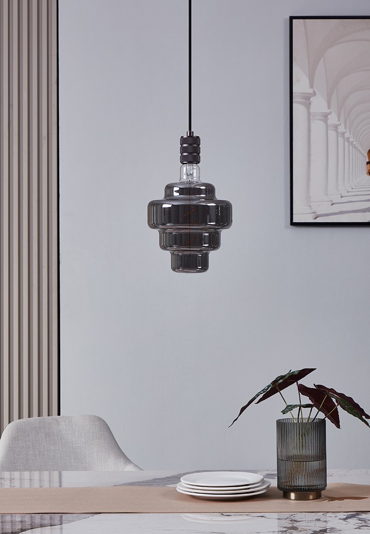 Transparente Glaspendelleuchte mit geschichtetem Design, dunkelgrauer Farbe und schwarzem Kabel, schwebend über einem Esstisch mit Tellern.