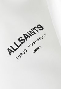 Bijela tkanina s podebljanim crnim tekstom koji glasi "ALLSAINTS" i "LONDON", s dodatnim tekstom na japanskom ispod.