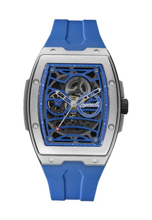 Montre automatique avec un bracelet en caoutchouc bleu, boîtier en acier inoxydable, cadran squelette, accents argentés et bleus, et marqueur triangulaire rouge.