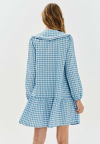 Modrá a biela kostkovaná šaty s dlhými rukávmi, volánovým golierom a rozšírenou sukňou. Vyrobené z ľahkého materiálu.
