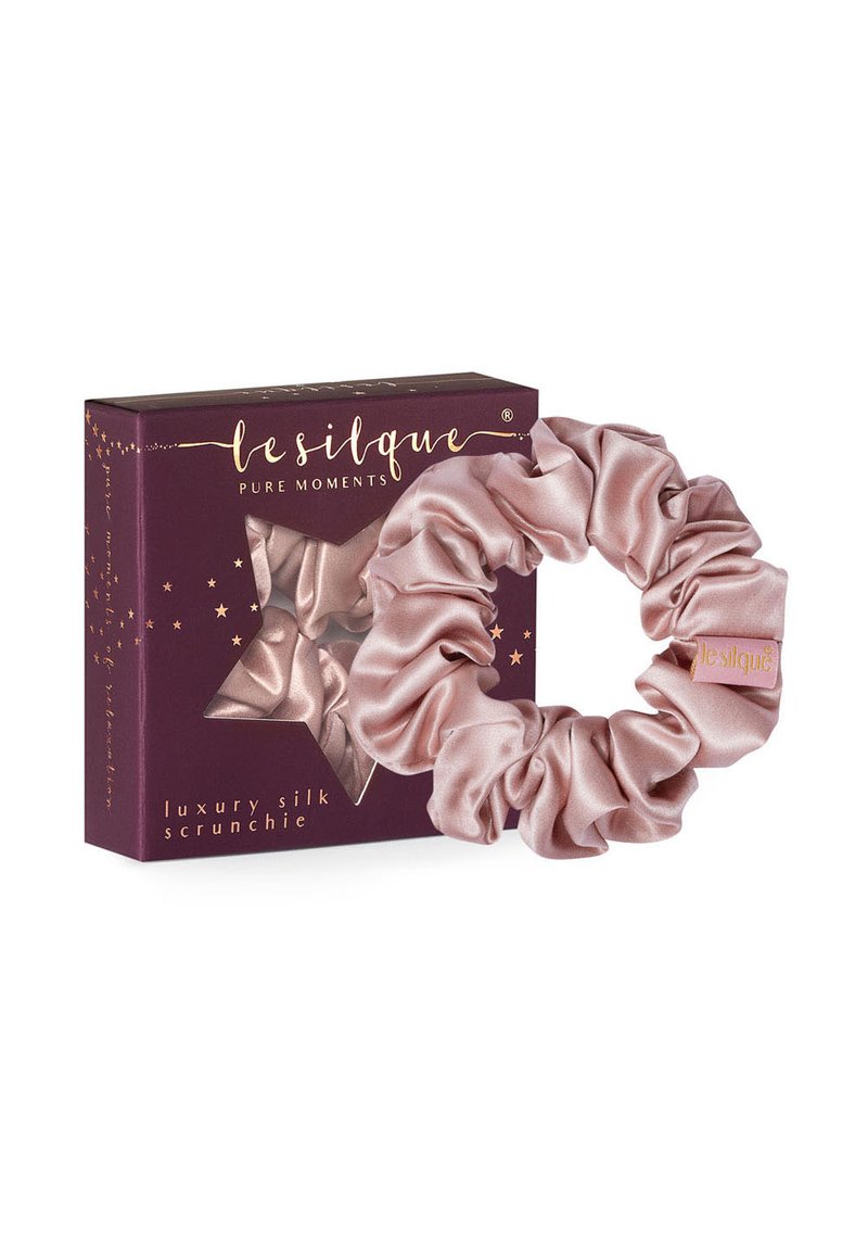 Luxueuze zijden scrunchie in zachtroze, met een gladde textuur en een volle, samengevoegde vorm. Verpakt in een donkerpaarse doos met gouden accenten.