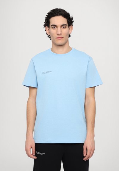 Lysblå bomulds T-shirt med korte ærmer, rund halsudskæring og små trykte tekstdetaljer på forsiden. Glat tekstur, afslappet pasform.