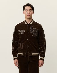 Brun manchester bomberjacka med beige detaljer, som har broderade lappar, knappstängning och randiga ribbade ärmslut och nederkant.
