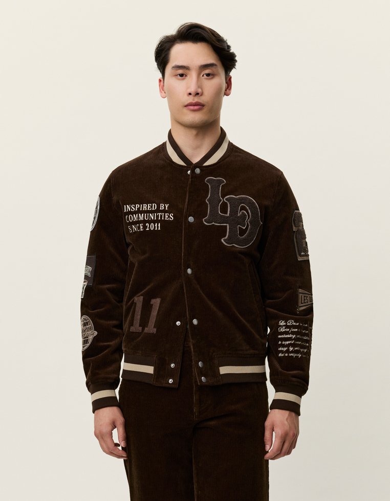 Brun manchester bomberjacka med beige detaljer, som har broderade lappar, knappstängning och randiga ribbade ärmslut och nederkant.