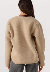 Beige fleece sweater met een gestructureerde afwerking en een ronde halslijn, voorzien van een bordeauxrode zoom en een losse pasvorm.