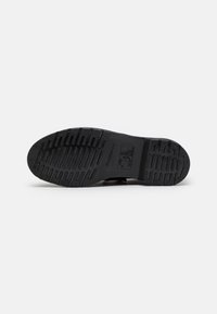 Suela de zapato de goma negra con patrones de textura, que presenta ranuras y secciones elevadas para mayor tracción, marcada con una impresión de logo.