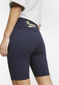 Marina cykelshorts i stretchmaterial med hög midja och en gyllene "Puma"-logotyp, slät yta och åtsittande design.