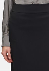 Svart blyertskjol med en slät, matt struktur. Midjebandet är platt och kombineras med en grå satinklänning med lång ärm, som visar upp en knappdetalj.