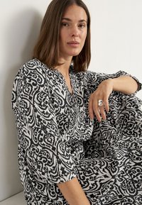 Schwarz-weiß gemustertes Kleid mit lockerer Passform, V-Ausschnitt und Dreiviertelärmeln. Verfügt über aufwendige Schwünge und eine fließende Textur.