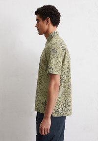 Korte mouw shirt in lichtgroene stof met bloemenprint in donkerblauw. Heeft een staande kraag en een relaxte pasvorm. Soepele textuur.