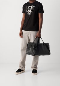 Černá kožená sportovní taška s zaoblenými okraji, dvěma držadly a zipovým uzávěrem, doplněná černým tričkem s grafickým motivem.
