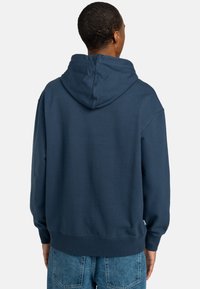 Navy blue hoodie with a large, adjustable hood, ribbed cuffs, and hem. Fabric appears soft and slightly textured. Standard fit design.