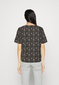 Blusa nera a maniche corte con un motivo floreale caratterizzato da piccoli fiori rosa e bianchi. Tessuto leggero con una vestibilità rilassata e scollo rotondo.