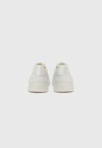 Baskets en cuir blanc avec une finition lisse, dotées d'une semelle légèrement surélevée et d'un branding subtil sur le talon. Couture rapprochée en accent.