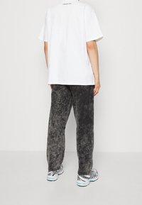 Przewymiarowany biały bawełniany t-shirt, szare dżinsy z efektem acid wash, czarne przeszycia oraz wzorzyste trampki z turkusowymi akcentami, widziane od tyłu.