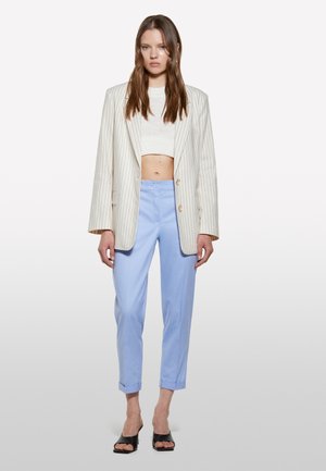 Blazer a righe crema sopra un crop top bianco, abbinato a pantaloni azzurri chiari arrotolati ai polsi e sandali a blocco neri con apertura sulle dita.
