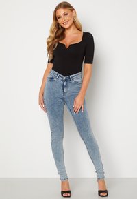 Body nero a maniche corte con scollo quadrato abbinato a jeans skinny blu chiaro a vita alta. Denim testurizzato, vestibilità slim e lunghezza alla caviglia.