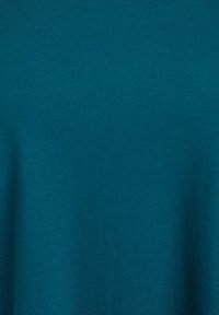 Turkizna bombažna majica z gladko teksturo in okroglim izrezom, z enotno barvo brez vidnih vzorcev ali akcentov.