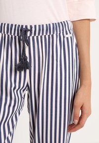 Marineblauwe en witte gestreepte broek met een elastische tailleband en een koord. Voorzien van decoratieve franjes aan de knoop en een comfortabele pasvorm.