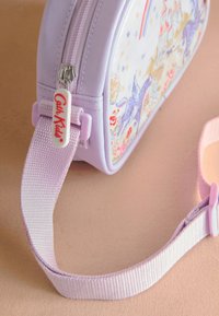 Liten lavendelfärgad axelväska med justerbar rem, dragkedjeförsedel märkt "Cath Kids" och färgglatt tryck med enhörning och slott på främre panelen.
