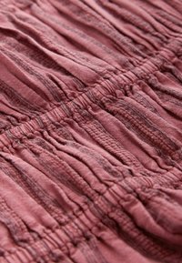 Close-up of textured dusty rose fabric with gathered, ruched stitching and subtle dark vertical stripes.