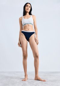 Witte sport-bh met groene en blauwe gestreepte band, gecombineerd met marineblauwe bikini-broekjes. Eenvoudig ontwerp met elastische taillebanden.