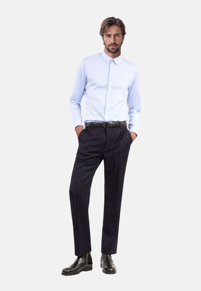 Helles blaues Langarmhemd mit Kragen, kombiniert mit navyblauen Nadelstreifenhosen und schwarzen Lederstiefeln. Schlichtes Design mit einem eleganten Look.
