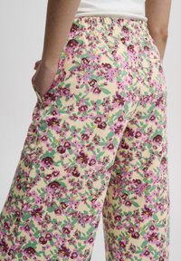 Pantalons à imprimé floral avec un fond crème et des fleurs roses et vertes, taille élastique et poches latérales. Tissu doux avec une coupe décontractée.