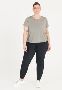 Grå kortärmad topp kombinerad med svarta leggings och vita sneakers. Toppen har en avslappnad passform och mjukt tyg; leggingsen sitter tajt.